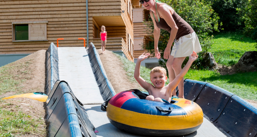 Das Foto zeigt eine Mutter die ihr Kind der Tubingbahn runter schiebt Das Foto zeigt eine Mutter die ihr Kind der Tubingbahn runter schiebt